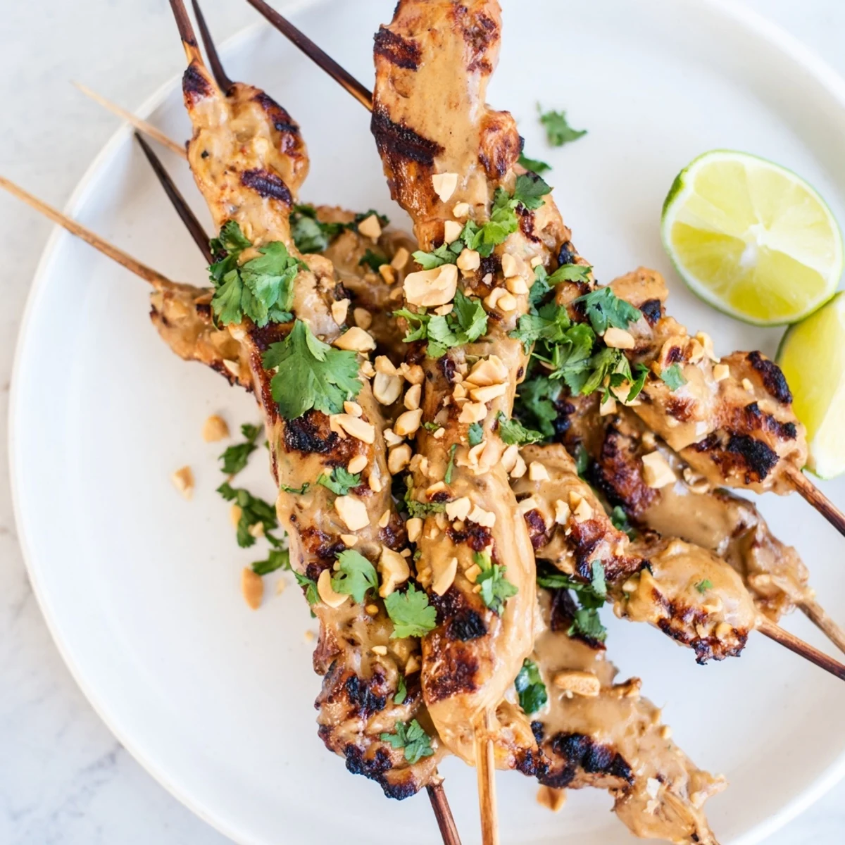 Tender grilled Chicken Satay Skewers with Peanut Sauce arranged on a platter with lime wedges.
