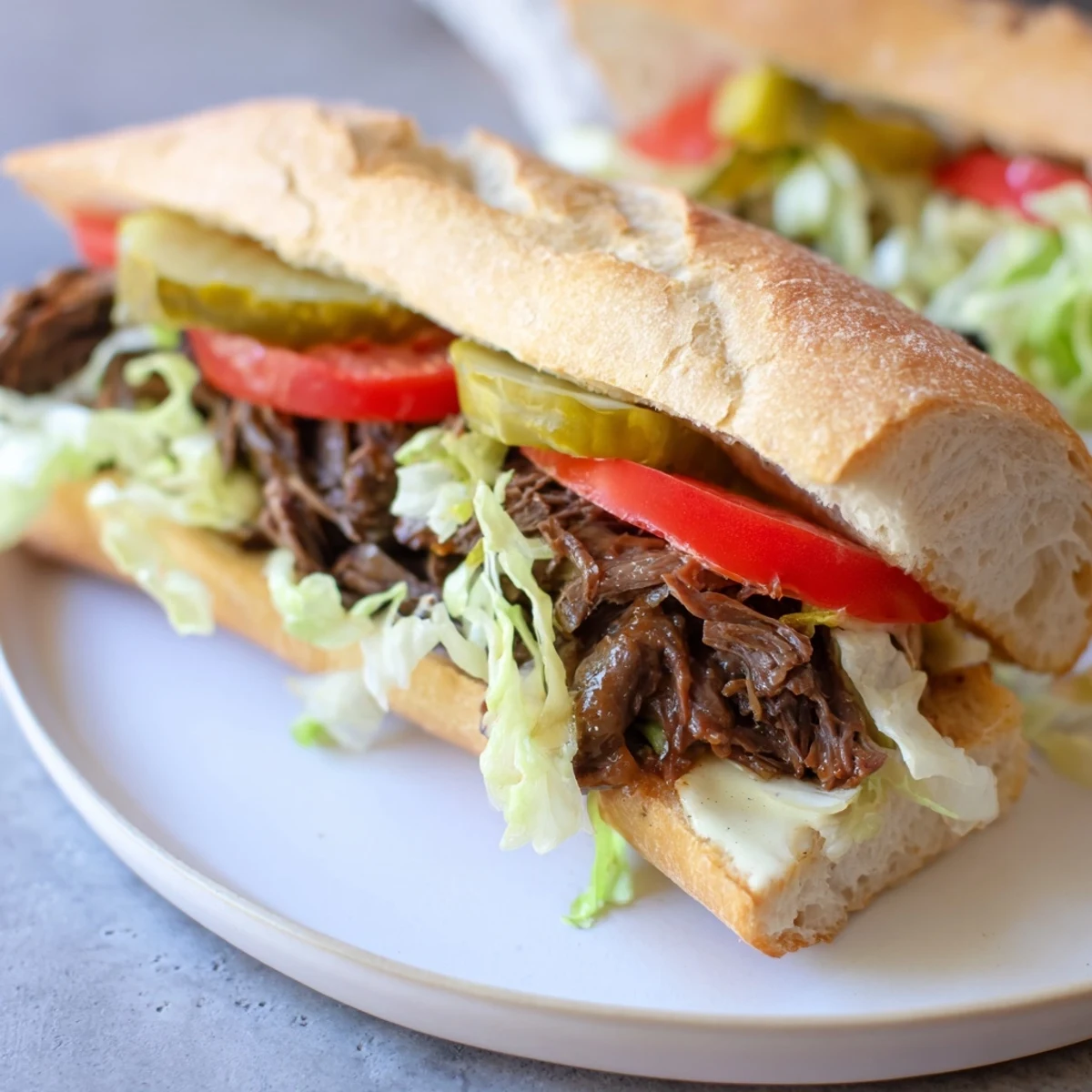 Close-up of a roast beef po boy sandwich drizzled with rich gravy, layered with juicy tomatoes and crunchy pickles on a toasted baguette.  