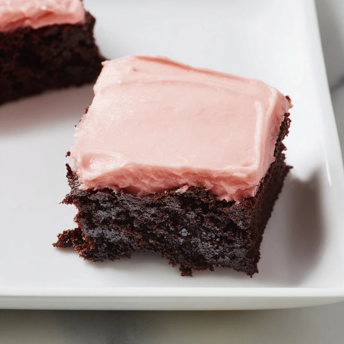 Moist, crackle-topped brownie squares are swirled with creamy pink frosting on a wooden serving board for an easy home bake.