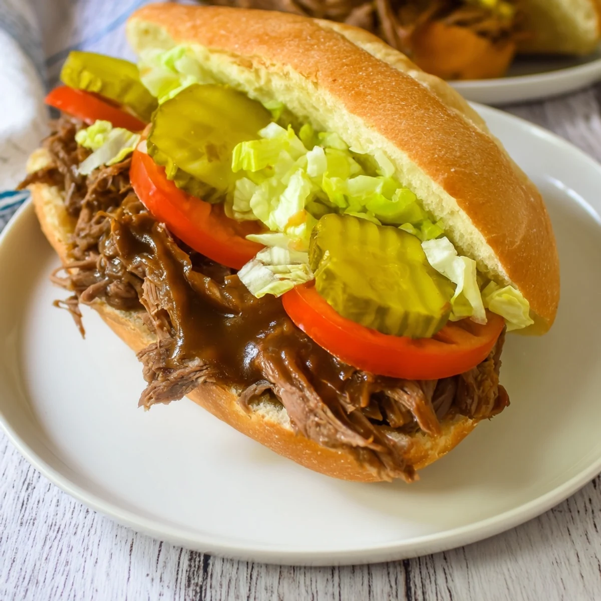 Freshly assembled Roast Beef Po Boy Sandwich with shredded beef, crisp lettuce, tomato, and pickles on crusty French bread.