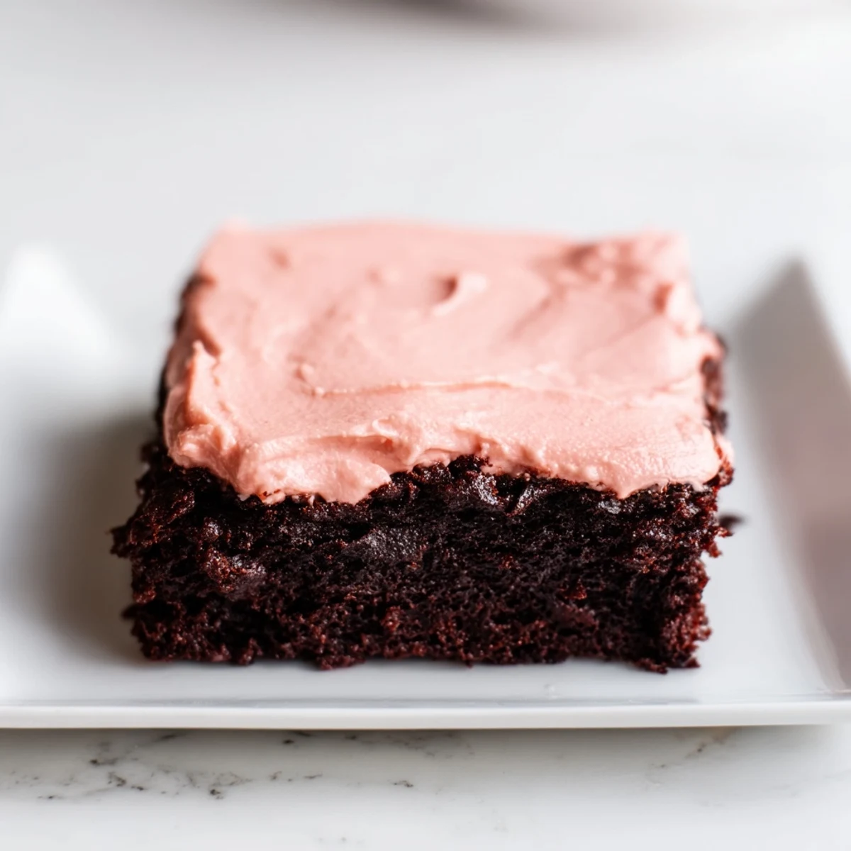 Freshly baked Brownies with Pink Frosting sitting on a wire cooling rack, showing fudgy edges and a vibrant, creamy pink topping.