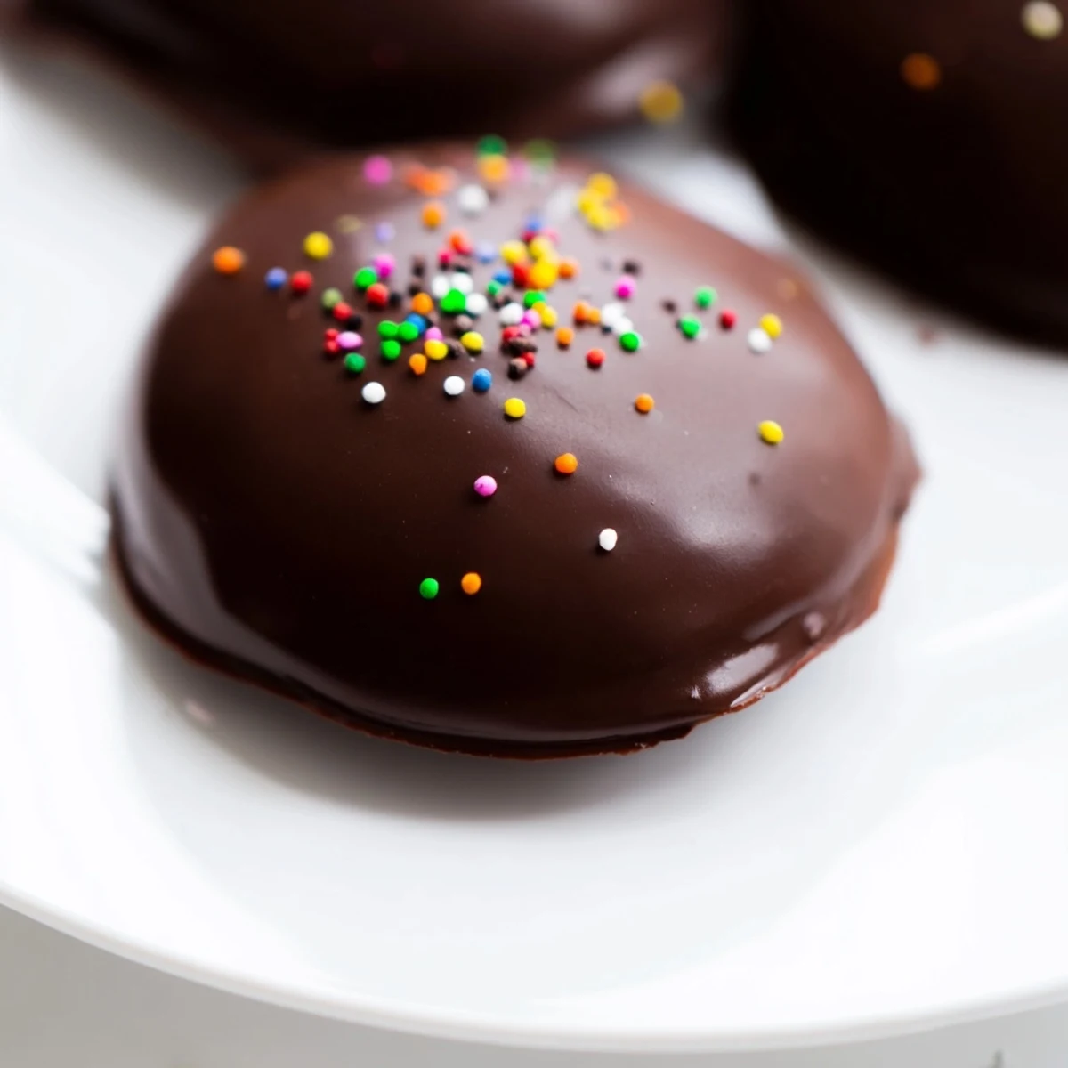 A close-up view of chocolate covered Peeps resting on parchment paper, showing rich cocoa sheen and optional nutty decorations.  