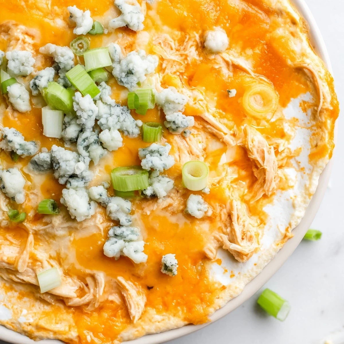 Golden bubbling Keto Buffalo Chicken Dip in a baking dish, topped with melted mozzarella and cheddar, served with celery sticks for dipping.