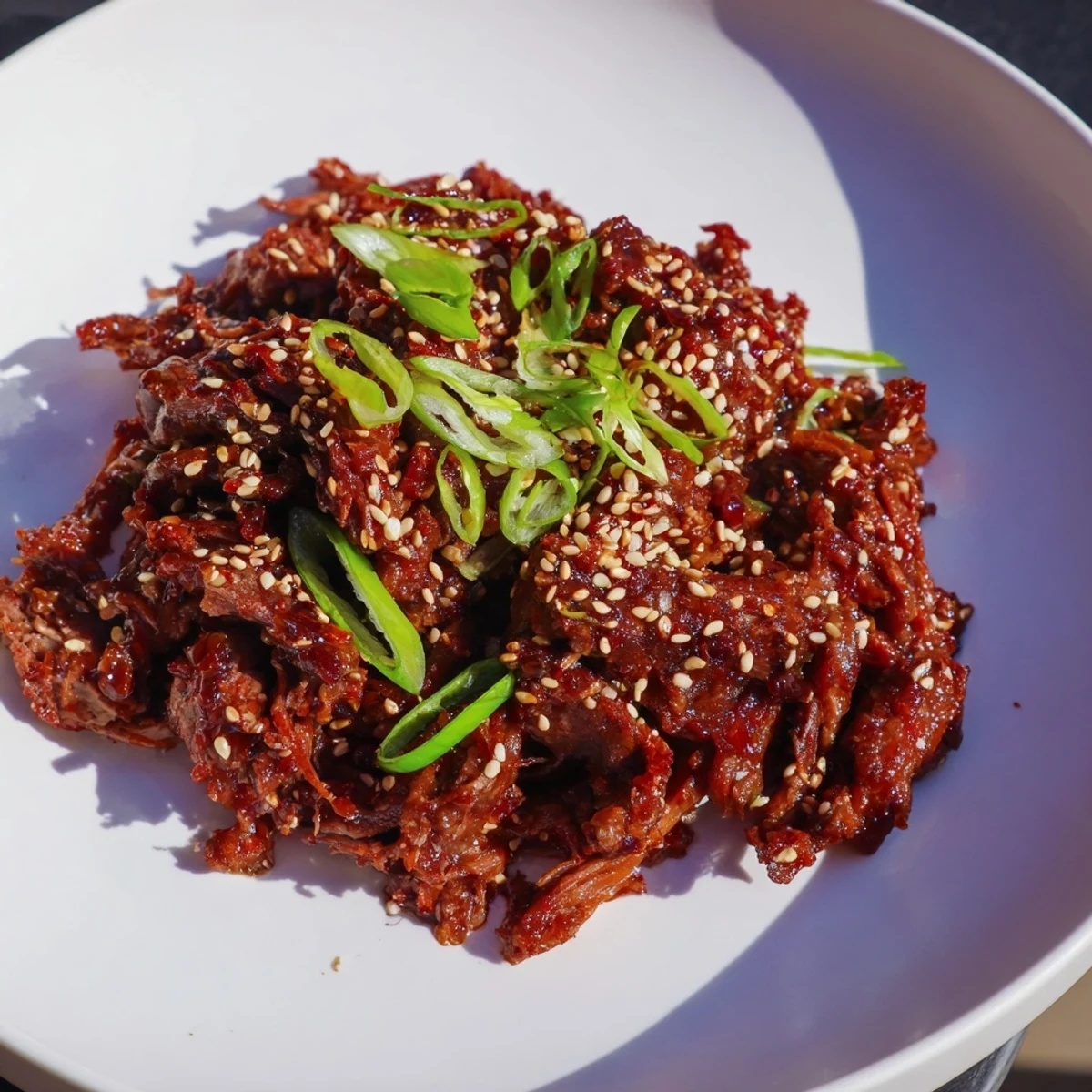 A bowl of Slow Cooker Korean Beef with tender meat, glossy sauce, and optional red chili slices on a rustic wooden table.