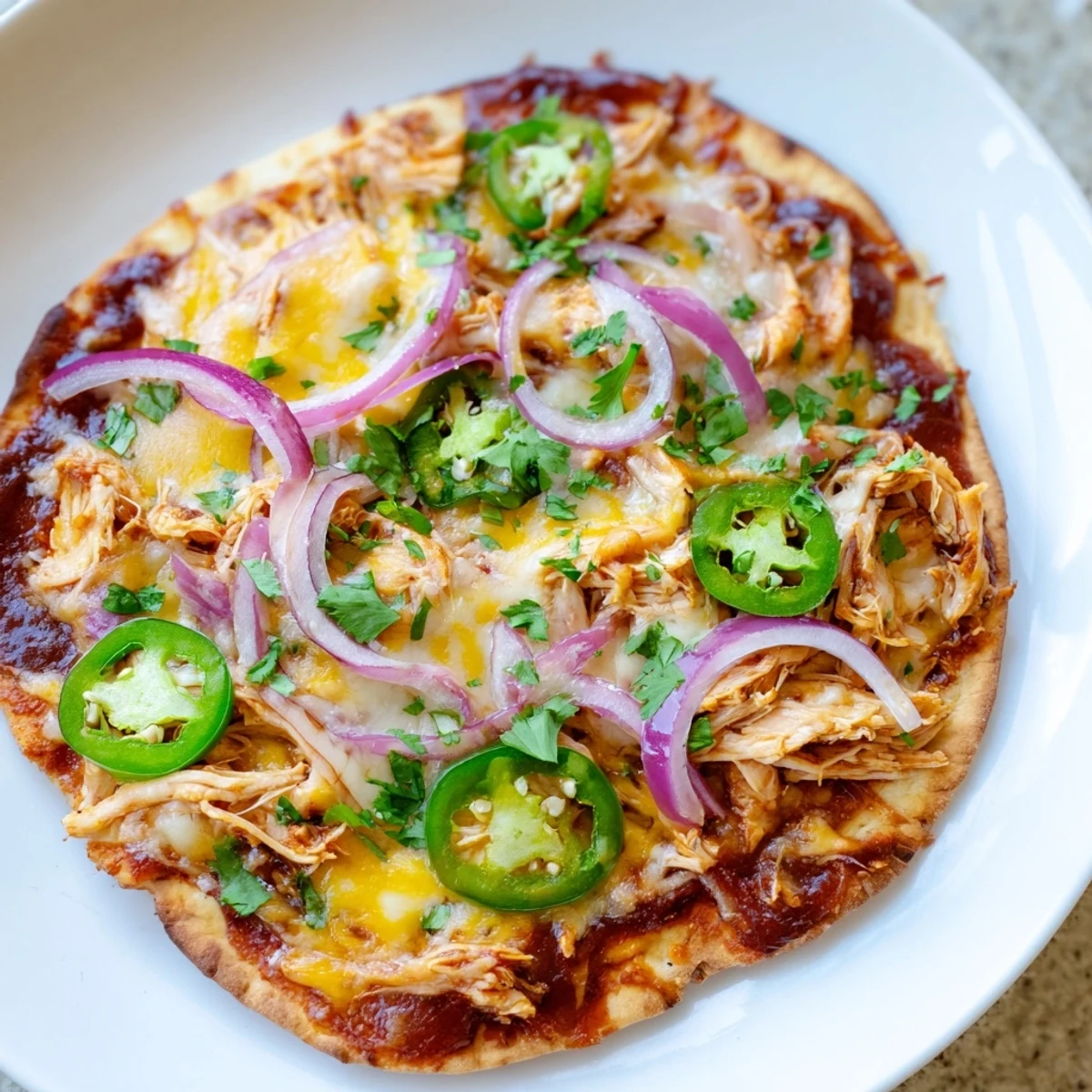 Sizzling BBQ Chicken Flatbread topped with melted mozzarella and cheddar cheese, fresh red onions, and jalapeños on a rustic naan base.