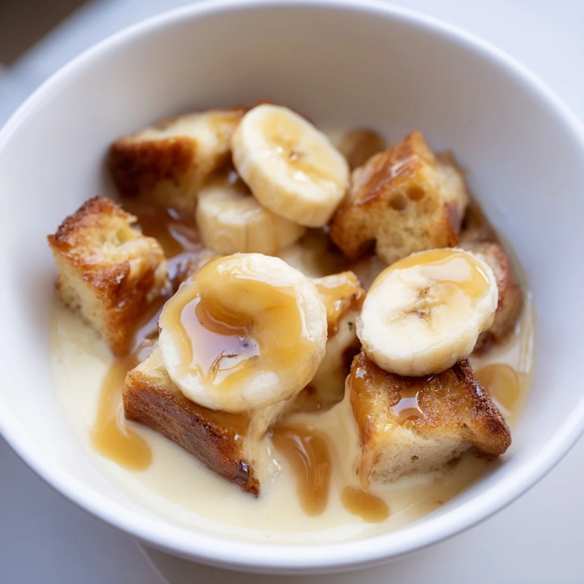Warm serving of creamy Bananas Foster bread pudding with caramelized banana slices and a scoop of vanilla ice cream melting on top.