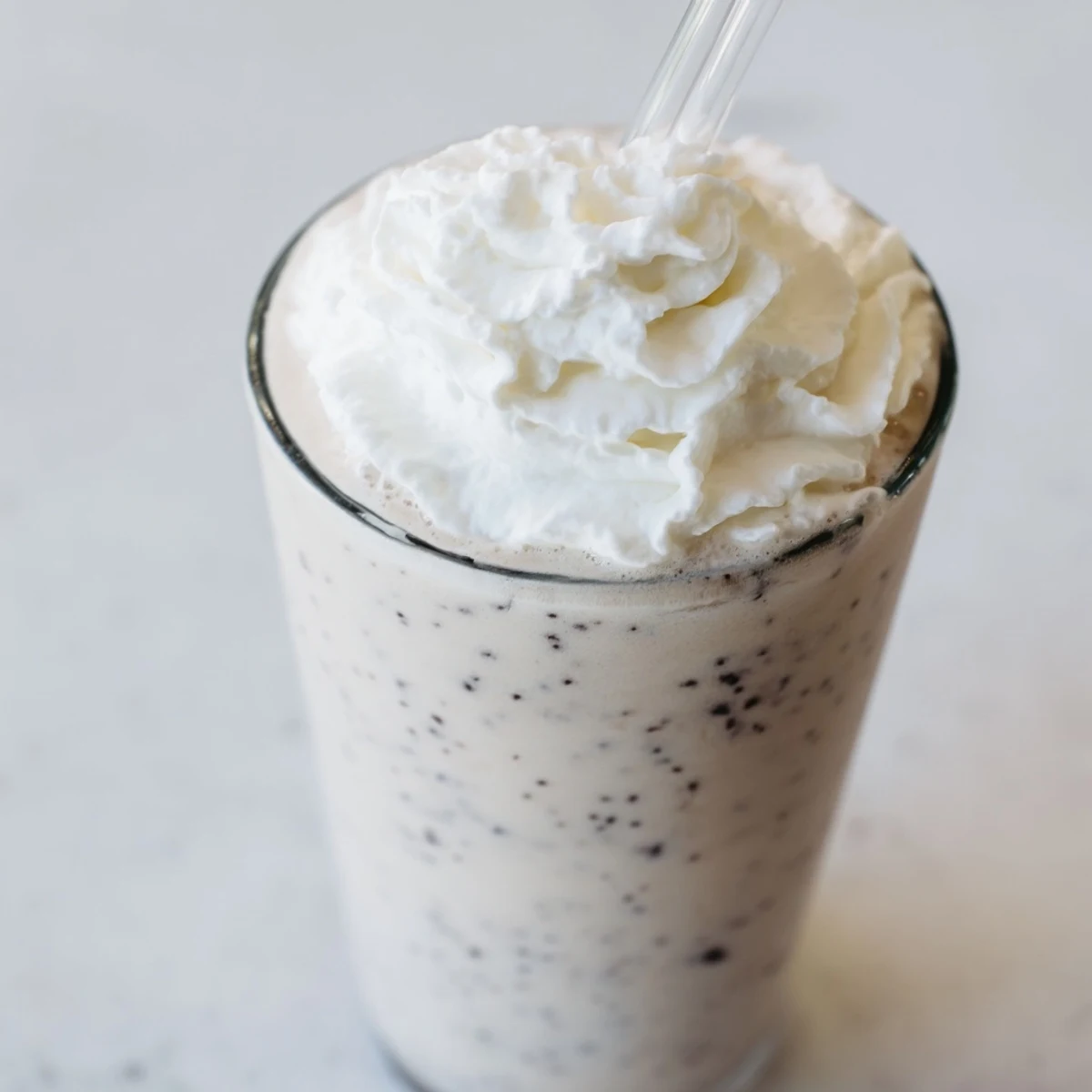 A tall glass of Vanilla Bean Frappuccino topped with whipped cream and a vanilla bean pod on the side.