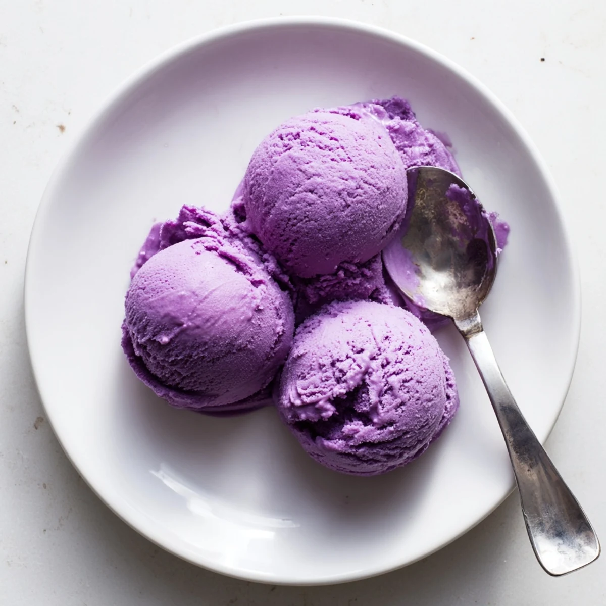 Vibrant purple Ube Ice Cream scoops glisten, topped with toasted coconut flakes on a chilled serving bowl.
