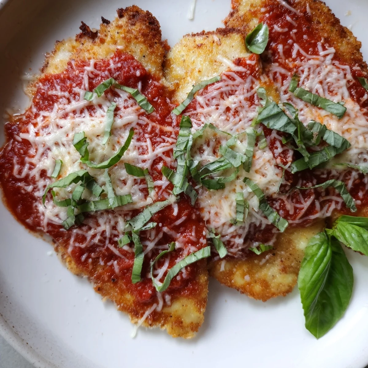 The Amazing 15 Minute Keto Chicken Parmesan rests on a white plate, featuring tender chicken, vibrant red sauce, and melted cheese garnish.