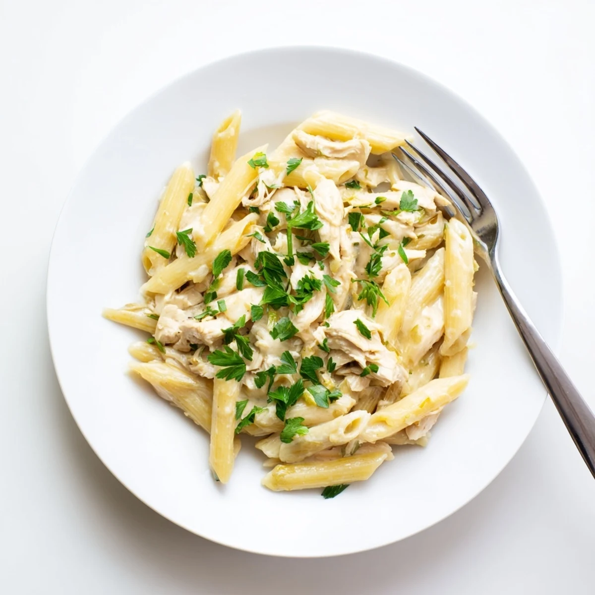 Golden shredded chicken and al dente Crockpot Garlic Parmesan Chicken Pasta in a rich, cheesy sauce, garnished with fresh parsley.
