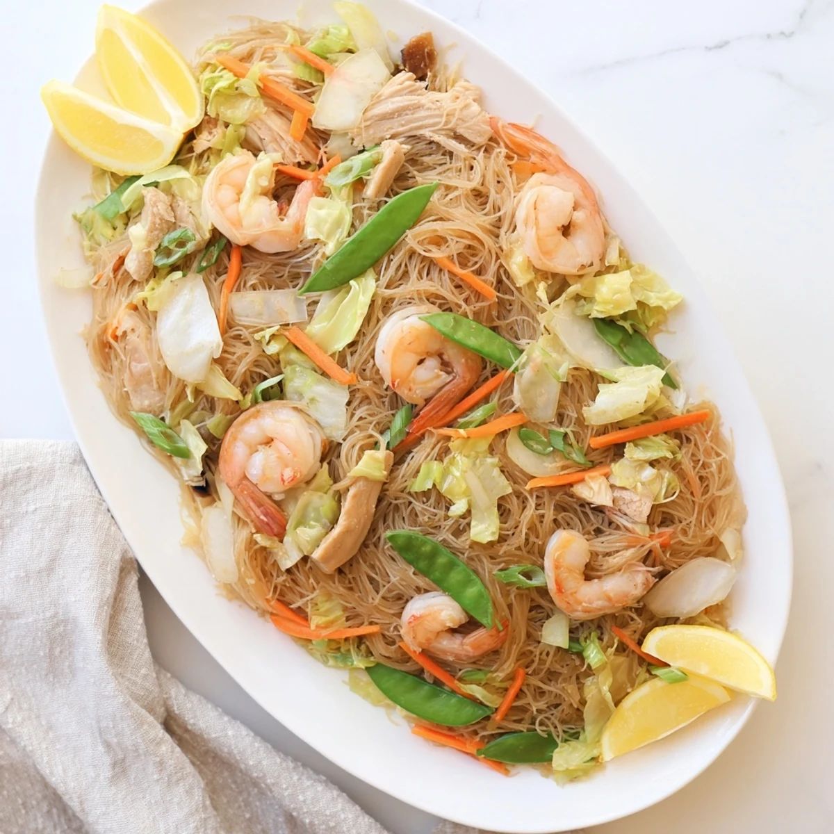 Golden plate of traditional Pancit Bihon topped with tender chicken, shrimp, and crisp colorful vegetables