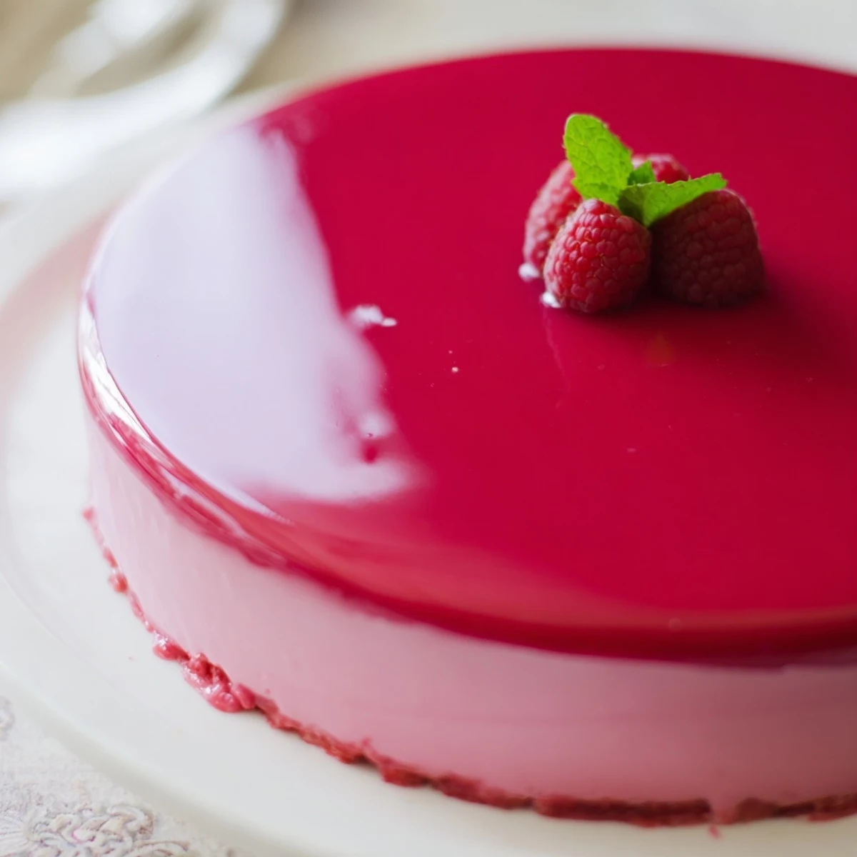 Elegant raspberry mousse cake with moist almond sponge layers and glossy red glaze
