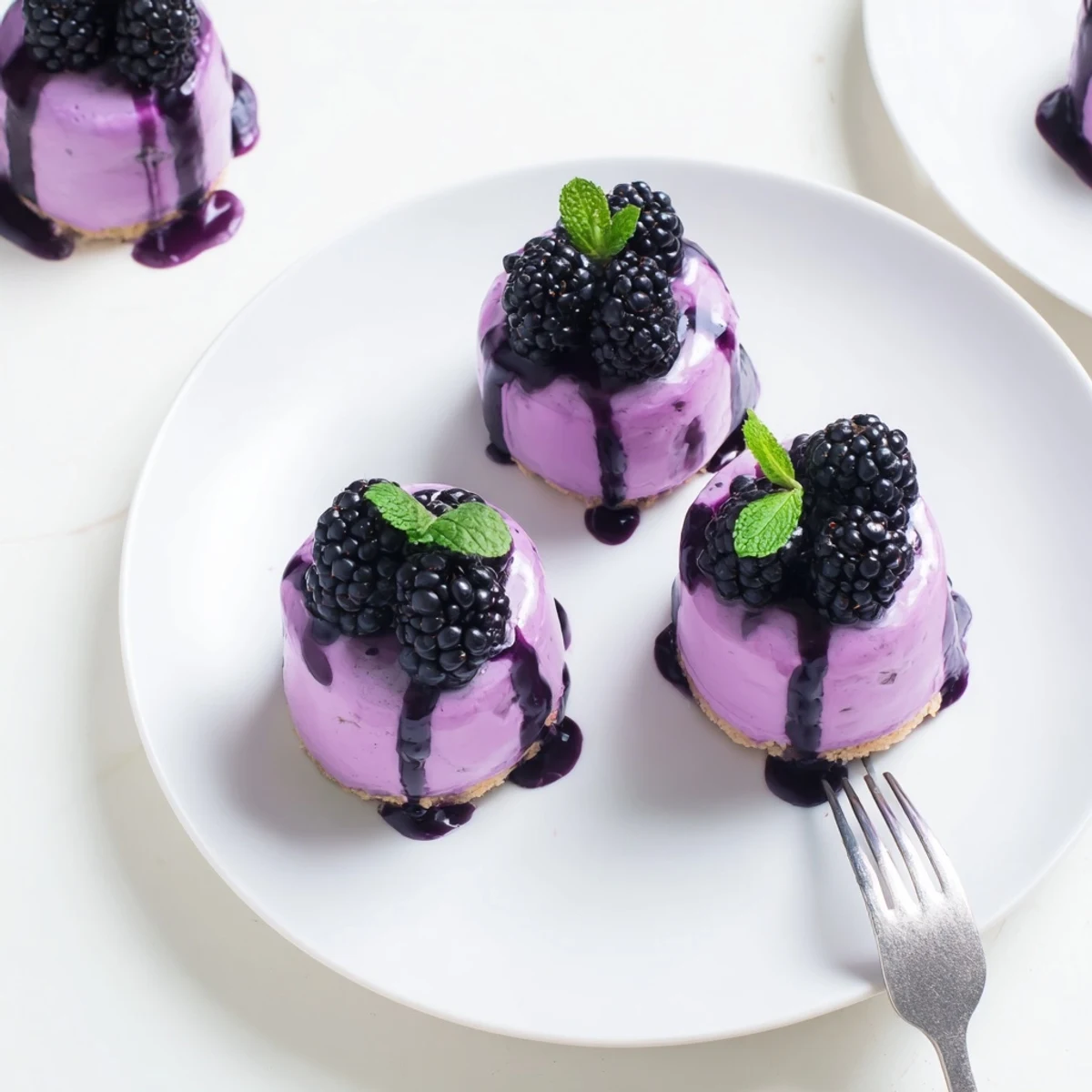 Glossy glazed mini cakes with fresh blackberry garnish on elegant white serving plate