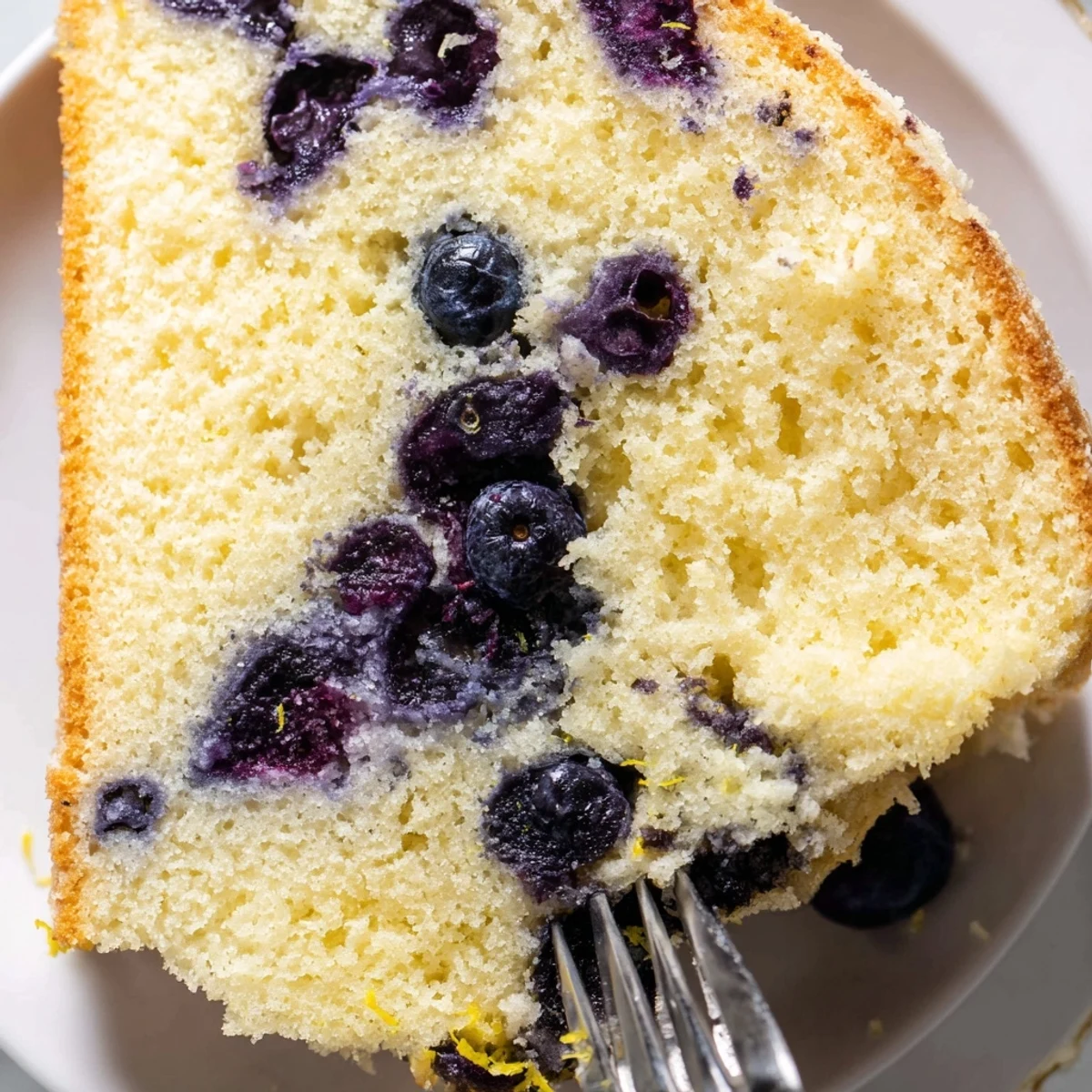 Golden slice of fluffy blueberry chiffon cake studded with fresh berries on a white plate