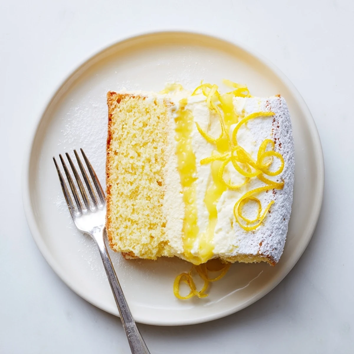 Two-layer Italian Grandmas Lemon Custard Cake dusted with powdered sugar and garnished with fresh lemon curl
