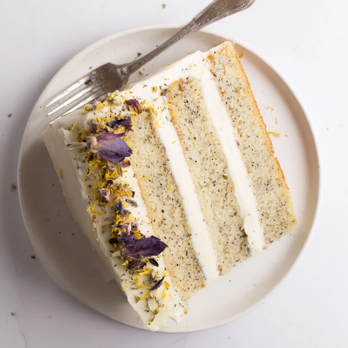 Three-tier London Fog cake garnished with lemon zest and edible flowers on white pedestal