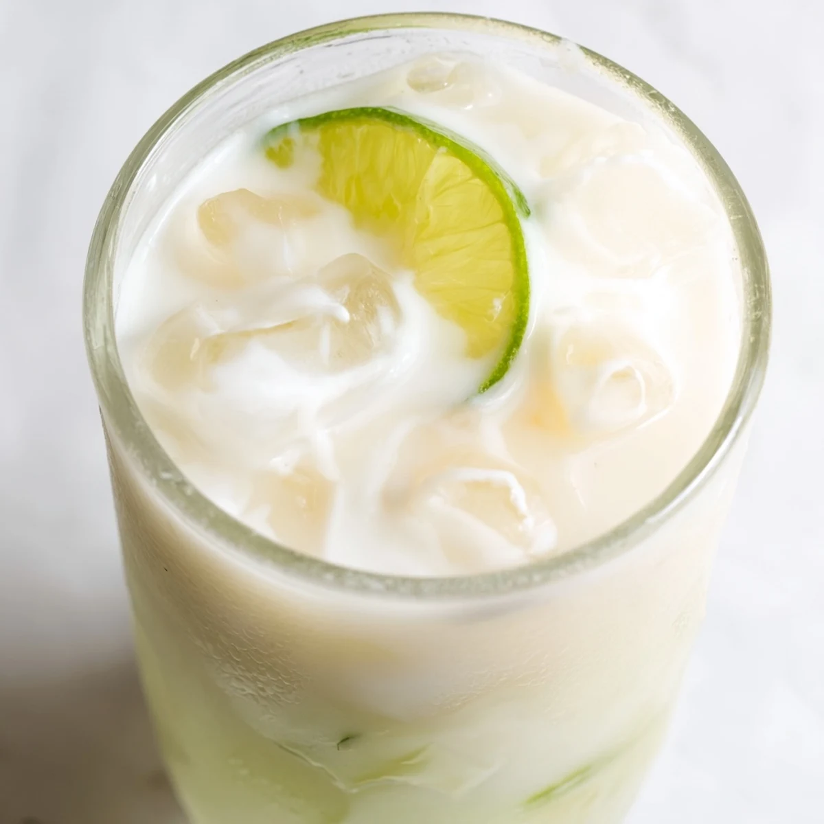 Frosty glass of creamy Brazilian lemonade garnished with fresh lime slices on ice