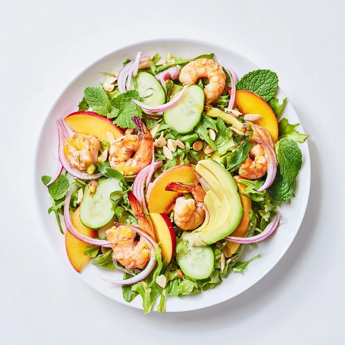 Colorful bowl of shrimp and nectarine salad topped with mint leaves and toasted almonds on mixed greens