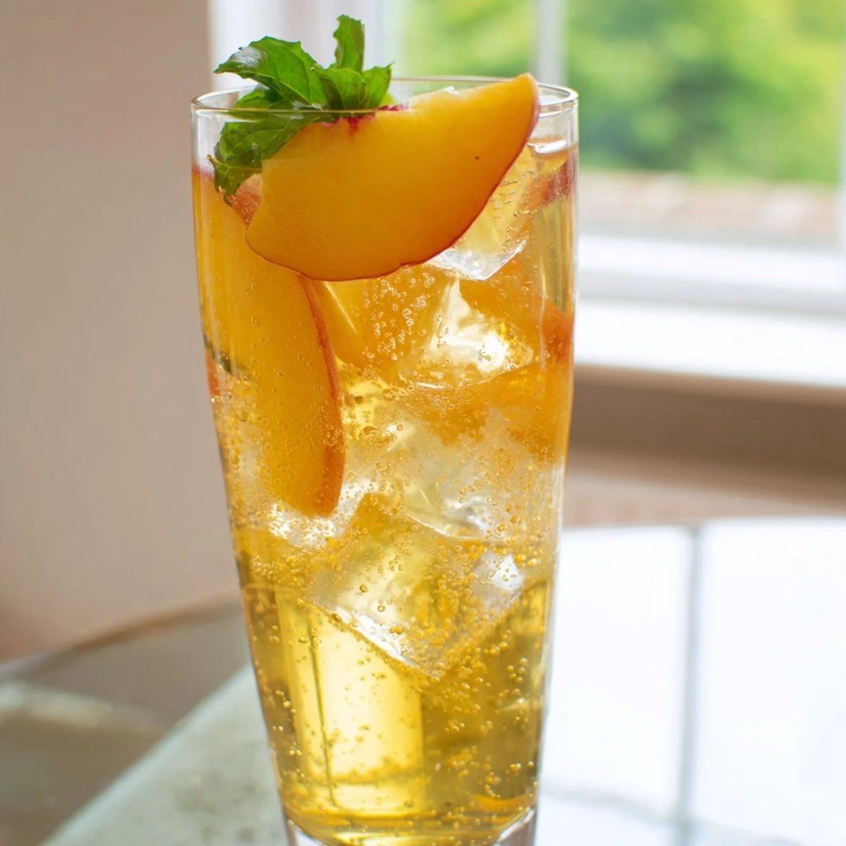 Golden Ginger Peach Sparkler served over ice in tall glasses with fresh mint sprigs and peach slice garnish on a sunny summer table