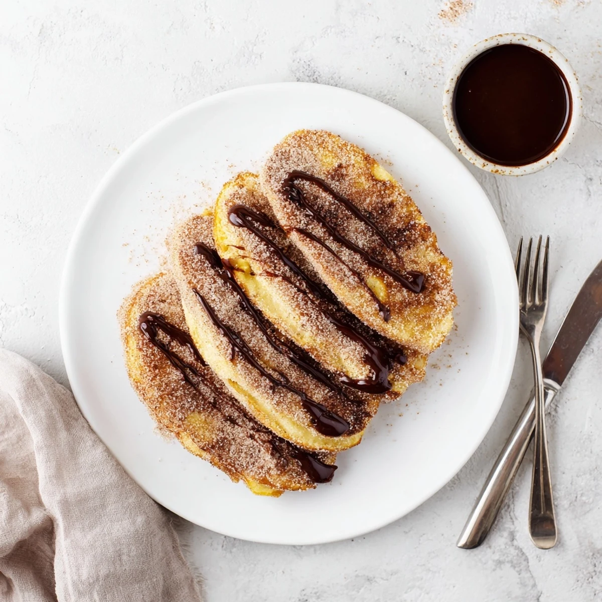 Fluffy Spanish Churro Pancakes stacked high with rich chocolate sauce drizzled on top