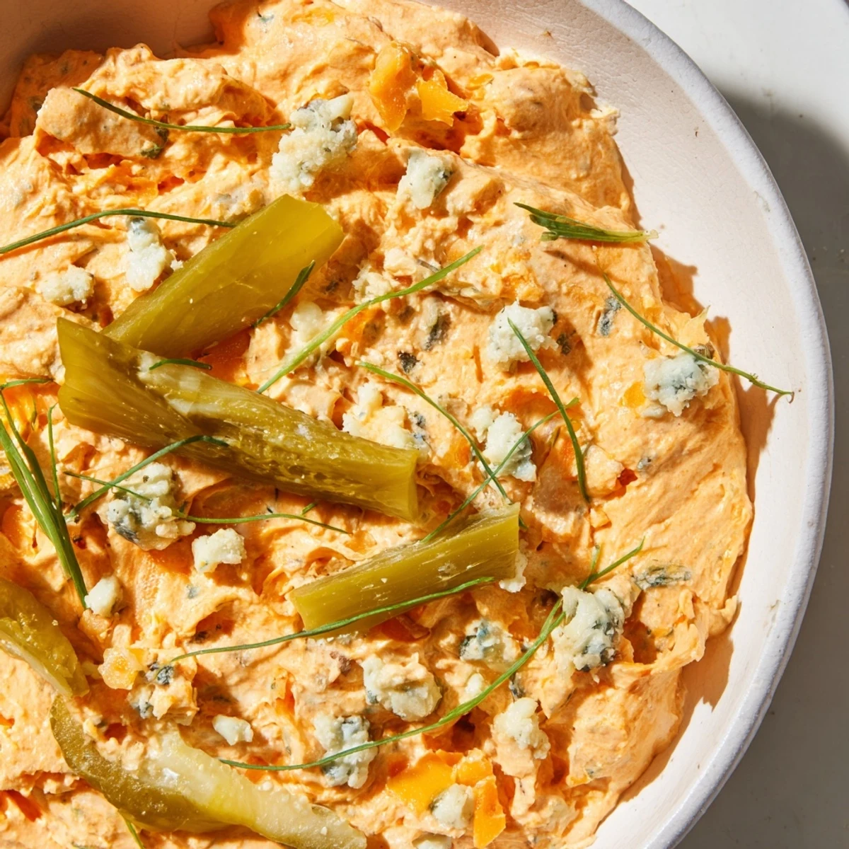 Creamy buffalo pickle dip in a serving bowl surrounded by crispy chips and fresh veggie sticks