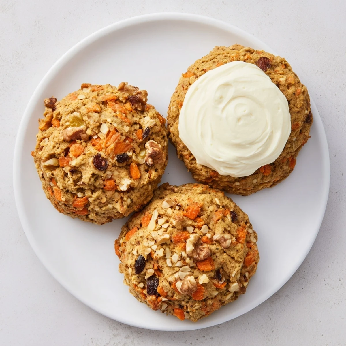 Golden carrot cake cookies topped with fluffy white cream cheese frosting on a wooden board