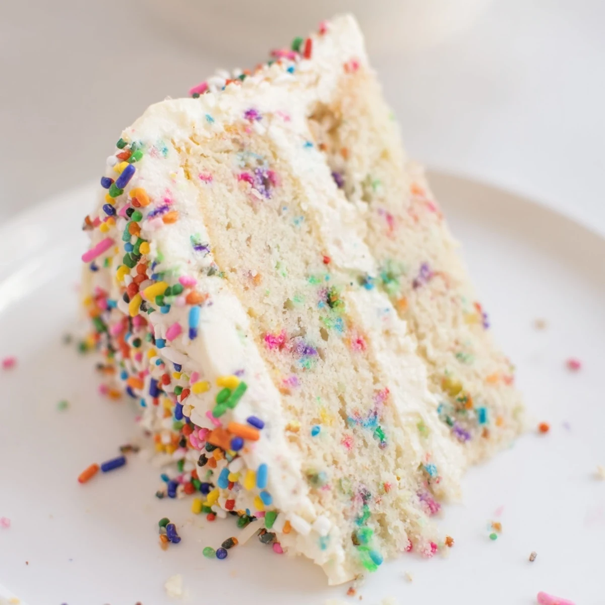 Slice of festive Funfetti cake showing bright sprinkles embedded in moist white cake with fluffy frosting