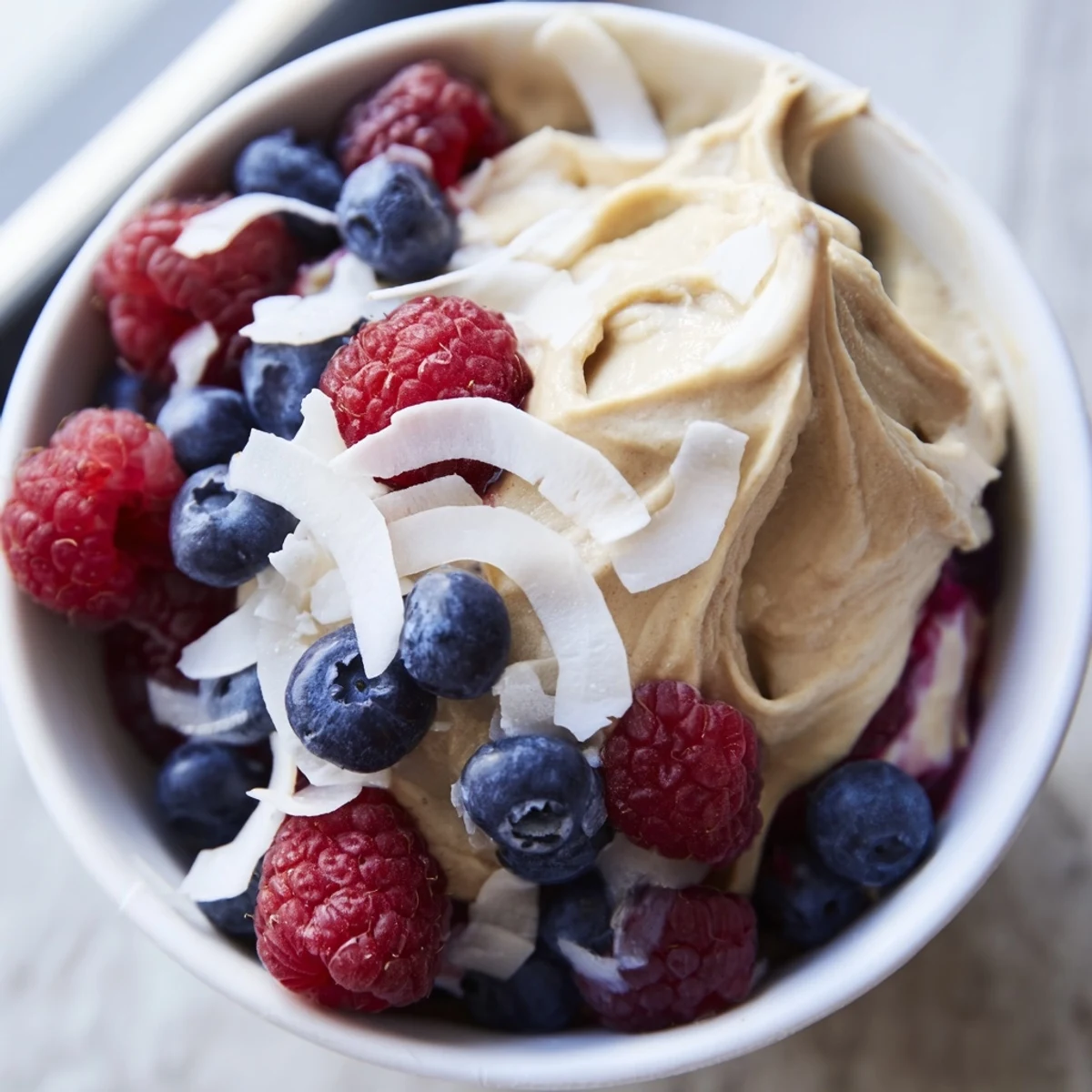 Frozen banana nice cream blended into smooth soft serve texture with dark chocolate chips and chopped nuts