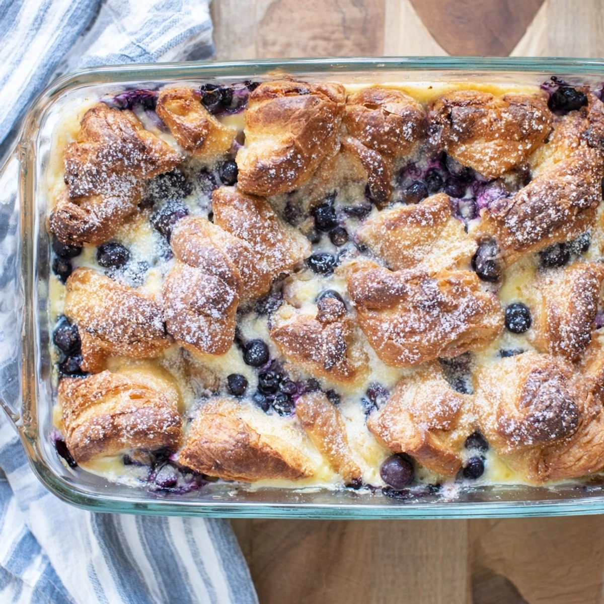 Golden blueberry cream cheese croissant casserole baked until bubbly with fresh berries scattered throughout