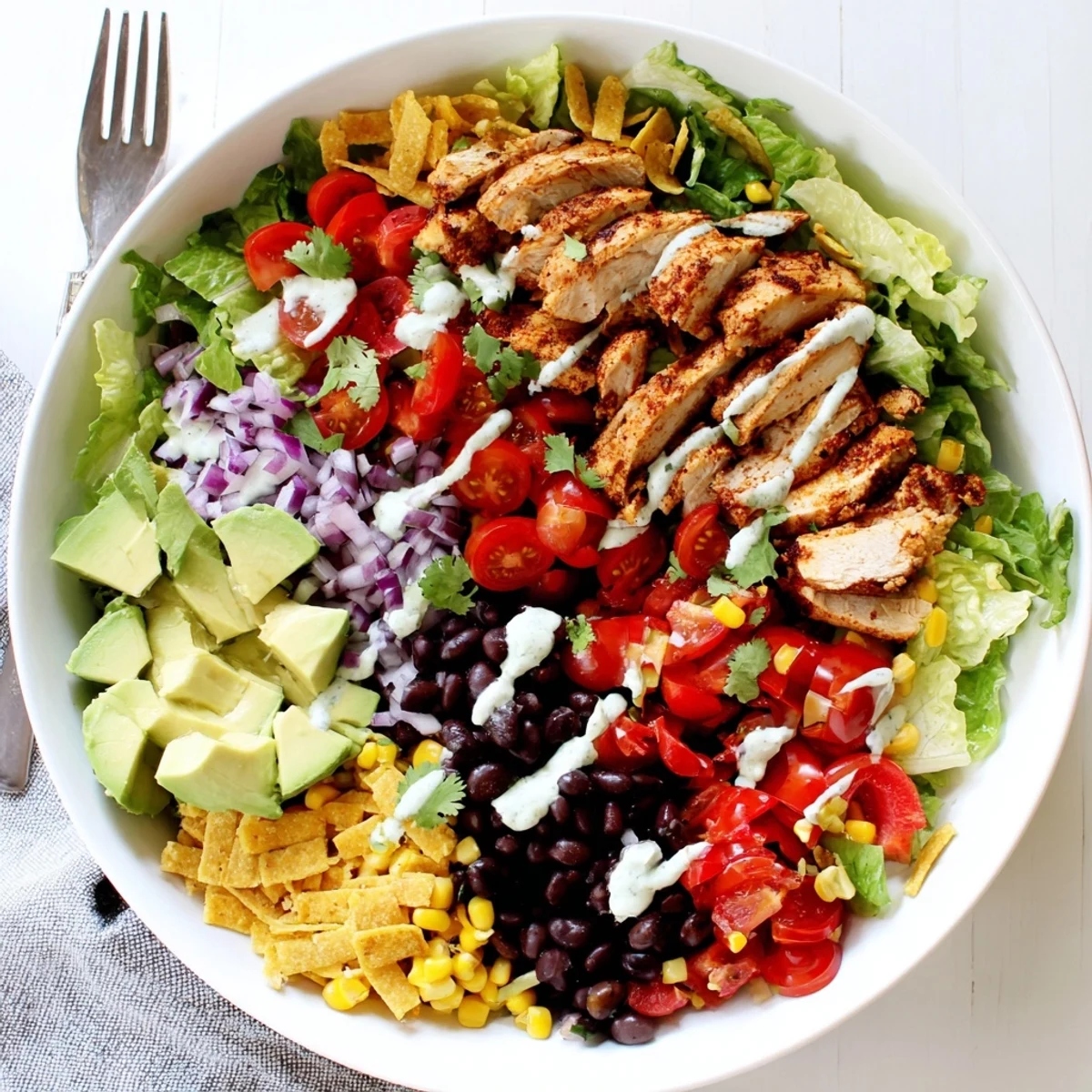 Colorful Southwestern chicken salad bowl topped with sliced grilled chicken, avocado, and creamy lime dressing