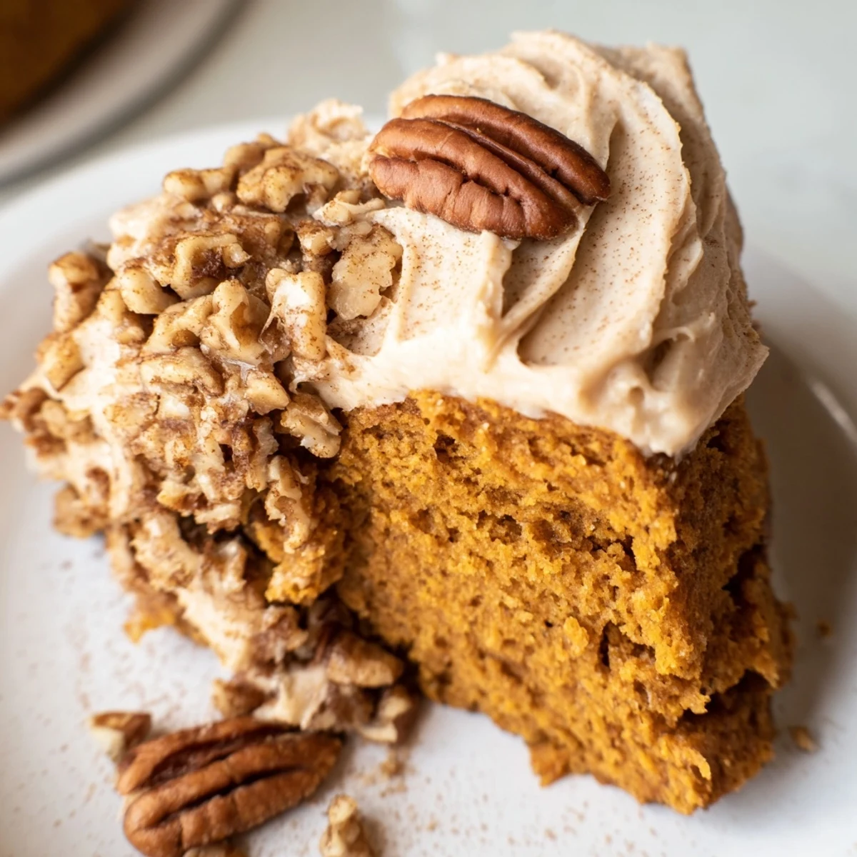 Frosted pumpkin pecan cake garnished with toasted pecan halves and a dusting of ground cinnamon