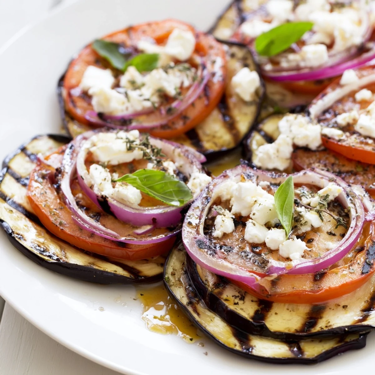 Golden charred eggplant and ripe tomato rounds stacked with fresh herbs on a rustic plate