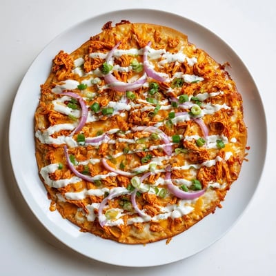 Freshly baked Bold Buffalo Chicken Pizza drizzled with ranch and extra buffalo sauce on a rustic wooden board.