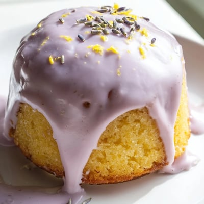 Mini lemon cakes with lavender glaze garnished with lemon zest on a cake stand