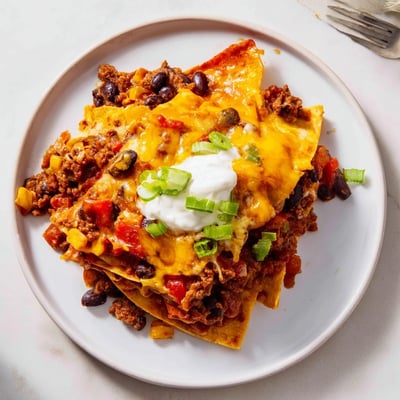 Beef Skillet Enchiladas topped with avocado, green onions, and creamy sour cream