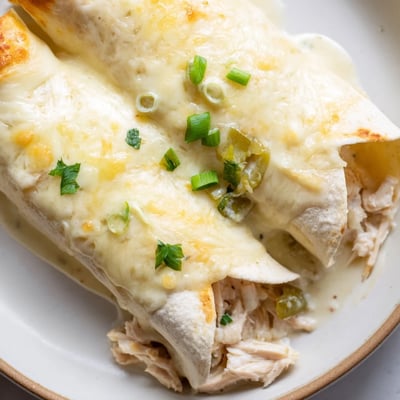 A slice of Creamy White Chicken Enchiladas plated with cilantro and lime wedge
