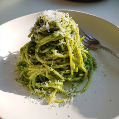 Wild garlic pesto pasta twirled on a fork topped with grated Parmesan cheese